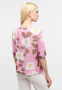 Kortærmet bluse i pink stof med et blomsterdesign, der har hvide blomster, brune blade og gule detaljer. Glat tekstur og løs pasform.
