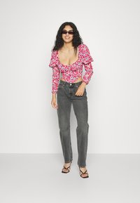 Top curto floral com mangas bufantes em rosa, vermelho e branco, combinado com jeans cinzentos de cintura alta e sandálias pretas de tiras.