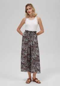 Un débardeur blanc à côtes associé à un pantalon ample de longueur genou avec un motif léopard noir et marron. Des sandales marron viennent compléter le look.
