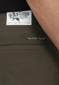 Groene katoenen broek met een wit label met het "volcom" logo en zwarte stiksels. Zakken aan de zijkant zichtbaar met contrasterende borduring van tekst.
