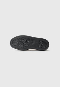 Crni gumenjak s teksturiranim uzorkom za prianjanje i logom "Converse All Star" na bijeloj pozadini.
