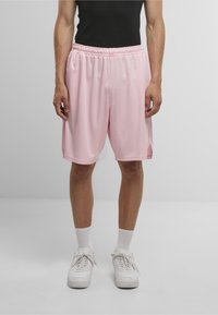 Lyserøde sportsshorts med elastisk talje og sidespalter, lavet af letvægtsmateriale. Båret med hvide sneakers og sokker.