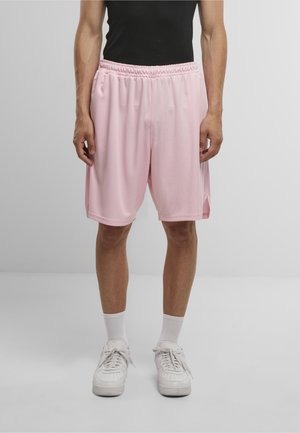 Lyserøde sportsshorts med elastisk talje og sidespalter, lavet af letvægtsmateriale. Båret med hvide sneakers og sokker.