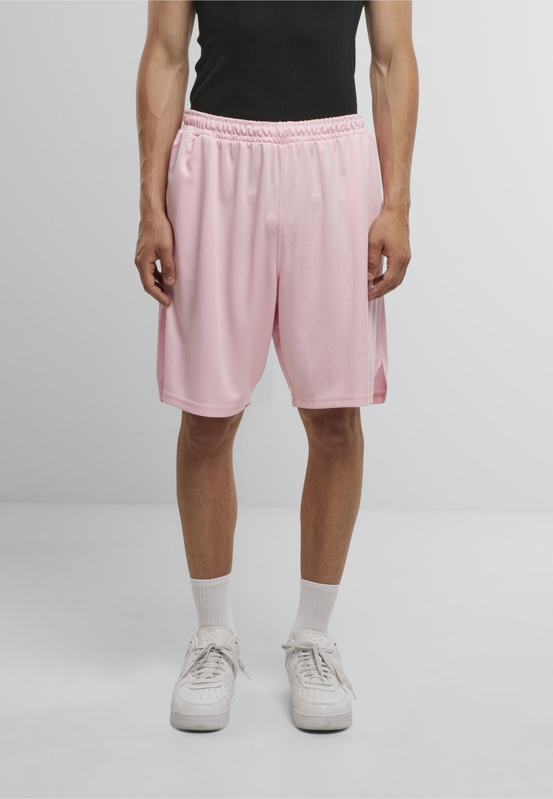 Lyserøde sportsshorts med elastisk talje og sidespalter, lavet af letvægtsmateriale. Båret med hvide sneakers og sokker.