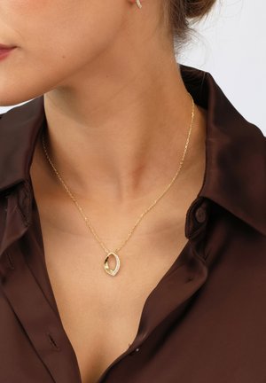 Goldfarbene Halskette mit einem ovalen Anhänger, der eine strukturierte Seite und eine Seite mit kleinen klaren Steinen geschmückt hat, die an einer filigranen Kette hängt.
