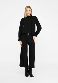 Must musta pikad varrukad blouse, millel on seotud kaeluse detail, koos laia jala mustade pükstega. Komplekti kuulub kitsas vöö metallklambriga.