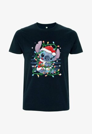T-shirt noir avec le personnage de dessin animé Stitch portant un chapeau de Père Noël, emmêlé dans des guirlandes lumineuses colorées, assis contre un fond rayé avec des étoiles.