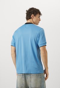 Polo shirt blu a maniche corte con finitura testurizzata. Presenta un colletto nero e cuciture a contrasto. Indossato con pantaloni shorts in denim chiaro.