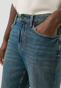 Dżinsy w jasnoniebieskim kolorze z lekko wyblakłą fakturą, zapinane na guziki i standardowymi szlufkami na pasek, z widoczną przednią kieszenią.