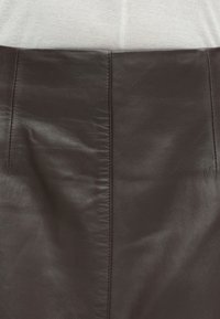 Brązowa skórzana spódnica o gładkiej fakturze, z centralnym szwem i subtelnymi detalami szewnymi. Prosty krój bez akcentów metalowych.