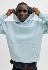 Sudadera con capucha azul claro con un bolsillo delantero y capucha ajustable. La tela parece suave con una textura lisa; presenta un ajuste holgado.