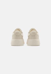 Beige skinnesko med høy bak, rund tå og tykk, lysfarget gummisåle. Minimal søm og ingen synlig branding.