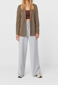 Bruin geruite blazer, grijze sweatpants met brede pijpen, gecombineerd met een cropped donkerrood topje. Heeft een gladde textuur en een neutraal kleurenpalet. Casual outfit.