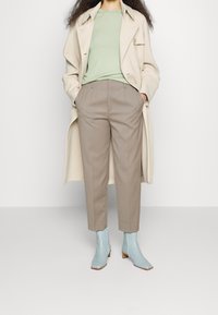 Beżowy płaszcz trencz, miętowy prążkowany sweter, spodnie w kolorze taupe o kroju na miarę oraz jasnoniebieskie botki na małym drewnianym obcasie.