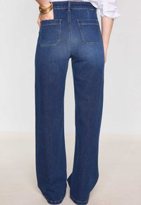 Jeans a vita alta e gamba larga in denim blu scuro. Presentano due tasche posteriori e cuciture a contrasto, con una vestibilità rilassata lungo le gambe.