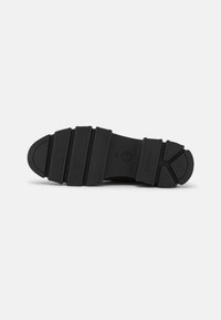 Suola di scarpa in gomma nera con scanalature orizzontali e un motivo testurizzato, caratterizzata da una punta arrotondata e un design robusto per la trazione.