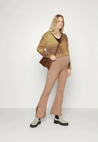 Cardigã tricotado em tons graduais de castanho, com botões e mangas longas; combinado com calças justas castanhas e botins verdes de tornozelo. Bolsa cruzada castanha.