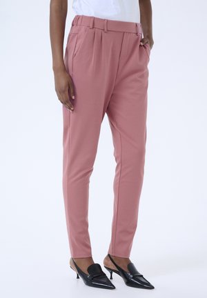 Pantaloni tailored rosa realizzati in tessuto morbido, con vita alta, pinces, tasche laterali e vestibilità slim. Indossati con tacchi a punta neri.