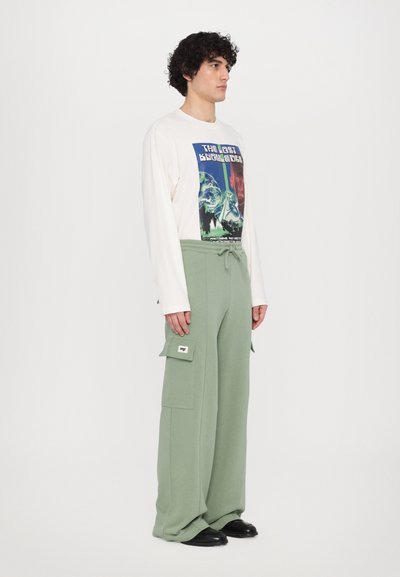 Light cream long sleeve shirt with graphic print, paired with loose-fit, olive green cargo pants featuring side pockets and drawstring.
