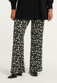 Uiteinde broeken in zwarte stof met een bloemenpatroon met witte en rode bloemen. Het ontwerp heeft een soepele textuur en een verlengd pasvorm.