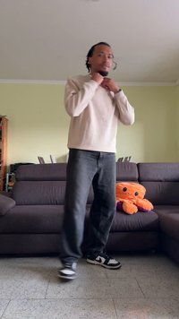 Top de mangas longas bege claro, jeans escuros e ténis preto e branco usados por uma pessoa numa sala de estar com um brinquedo de polvo laranja suave.