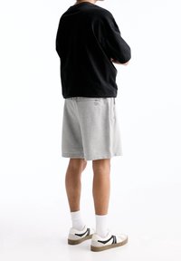 T-shirt noire oversized, shorts en coton gris, baskets blanches avec des accents noirs et chaussettes blanches, vus de l'arrière.
