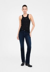 Top senza maniche nero con dettagli decorativi, abbinato a jeans in denim blu scuro e stivali neri alla caviglia. Tessuto morbido, design aderente.