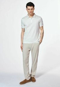 Biała polo koszulka z krótkim rękawem i kołnierzykiem, jasne lniane spodnie oraz brązowe zamszowe buty wsuwane. Prosty i minimalistyczny design.