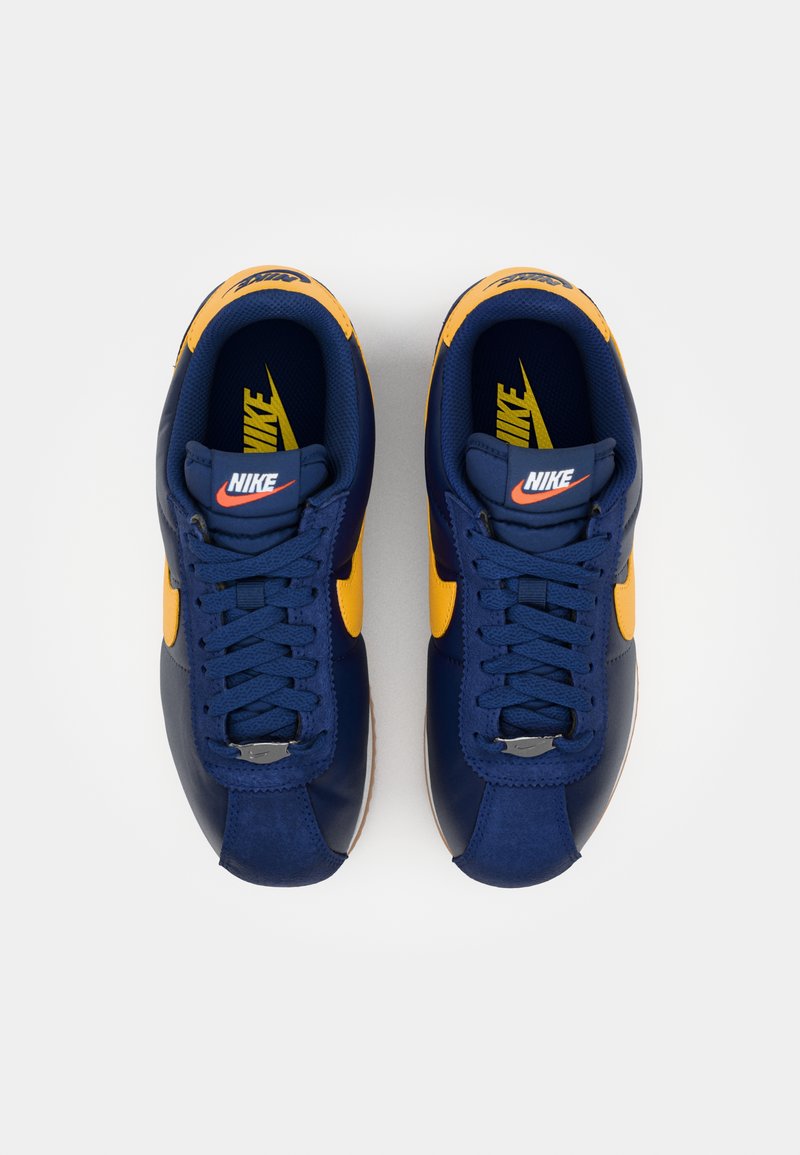 Les baskets Nike présentent un upper majoritairement bleu marine, des accents jaunes et une finition texturée. Elles comprennent un laçage traditionnel et un design classique.