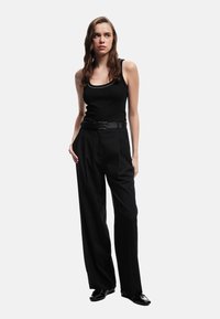 Top sin mangas negro con canalé y ribete plateado, combinado con pantalones de pierna ancha negros de cintura alta y un cinturón negro. Zapatos negros brillantes.