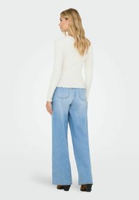 Witte geribbelde langemouwen top met golvende zoom, gecombineerd met lichtblauwe wijde denim jeans, met een soepele textuur en minimale stikdetails.