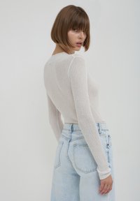 Top a maniche lunghe a coste in beige chiaro, abbinato a jeans azzurri a vita alta, caratterizzati da una vestibilità rilassata e tasche posteriori.