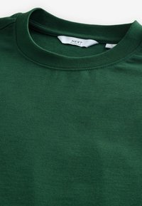 Camiseta de algodón verde con un ajuste relajado, con cuello redondo y textura suave y uniforme. Etiqueta visible dentro del cuello.