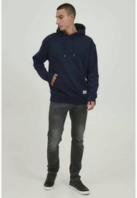 Navy blue hoodie with a drawstring, kangaroo pocket, ribbed cuffs, and hem; worn with gray jeans and black sneakers. Simple, clean design.