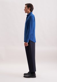 Camicia blu a maniche lunghe in tessuto textured, con colletto button-down e fessure laterali. Abbinata a pantaloni neri sartoriali e scarpe nere.