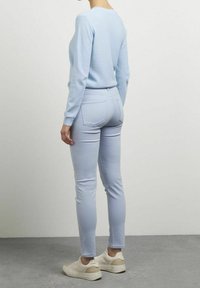 Jasnoniebieski sweter i dopasowane skinny jeansy z gładkiego materiału, uzupełnione beżowymi sneakersami. Prosty design z minimalnymi detalami.