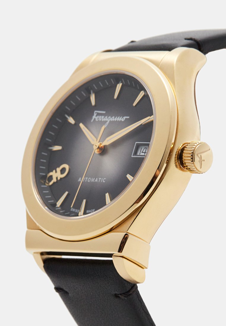 Montre automatique dorée avec un cadran noir, des accents argentés et un bracelet en cuir noir. Affiche la date et possède des index horaires bien marqués.