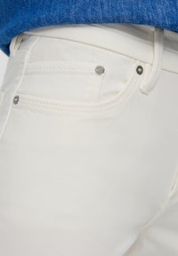 Białe dżinsy typu denim o klasycznym wzorze z srebrnymi nitami, podwójnym przeszyciem i średnim stanem. Widoczna kieszeń wewnętrzna z przodu.