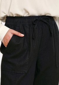 Černé kalhoty na stažení s texturovaným povrchem, mají boční kapsy a elastický pas. Materiál vypadá lehce a měkce.