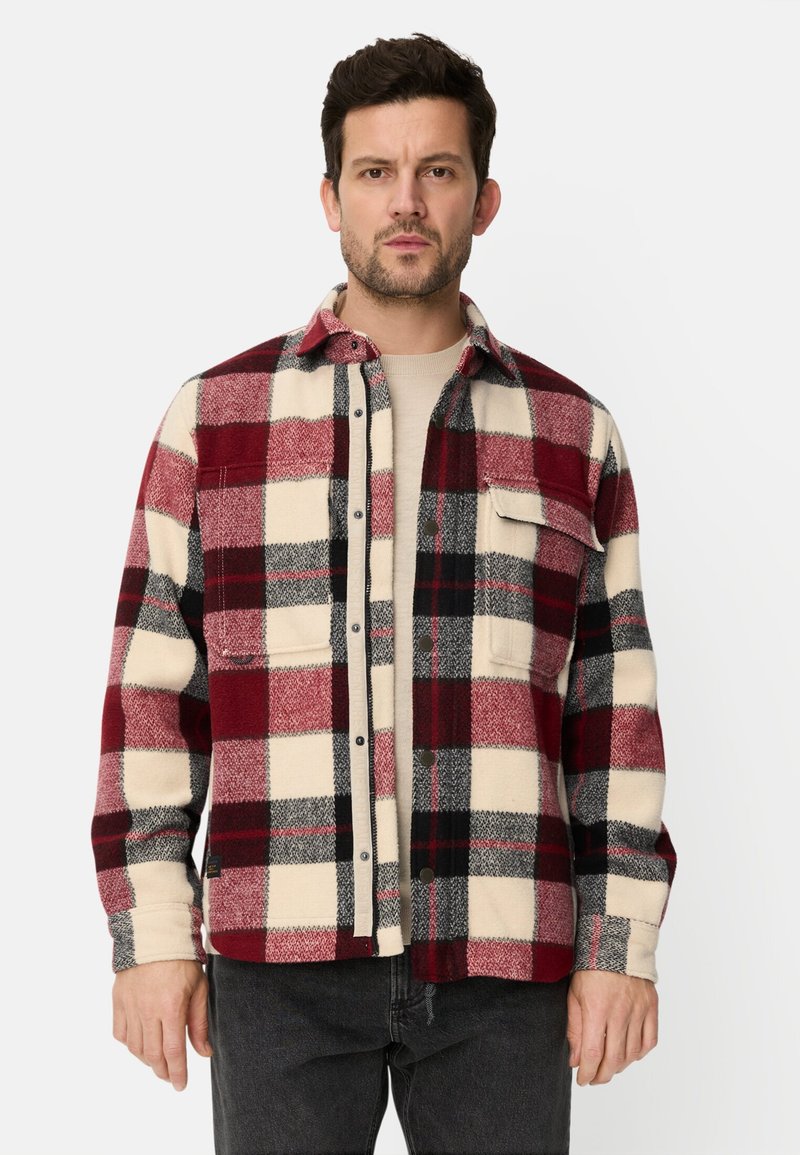 Rutet flannelskjorte i røde, sorte og cremefarver. Lavet af blødt stof med knapper foran og to brystlommer.