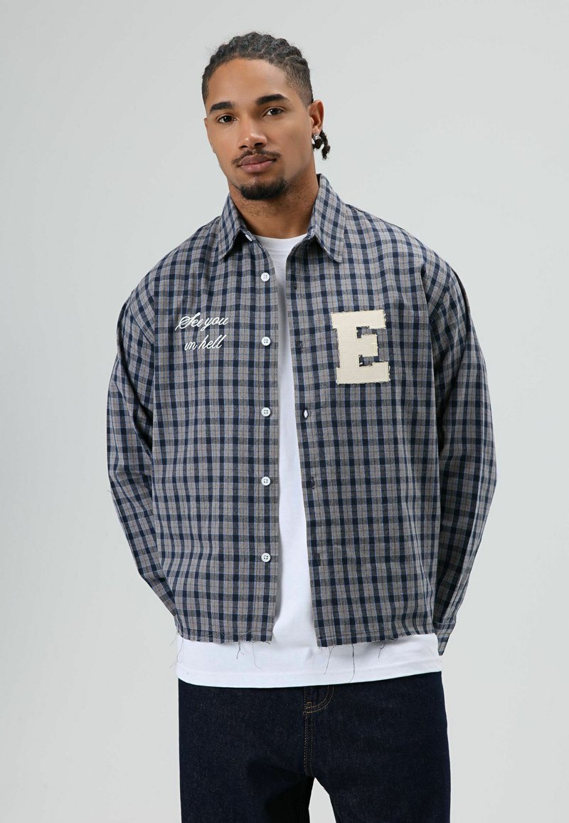 Geruit overhemd met lange mouwen in blauw en grijs katoen, met een wit geborduurde tekst en een beige stoffen letter "E" op de borst.