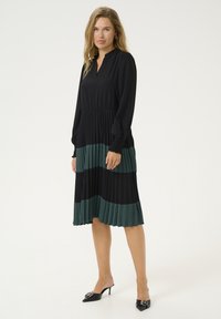 Melnas un tumši zaļas svārku kleitas ar apkakles kaklu un garām piedurknēm. Iespējo kontrastējošas horizontālas svītras un elastīgu jostas detaļu.