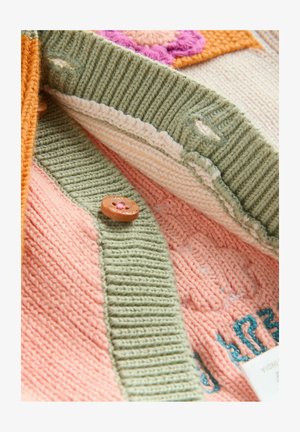 Horgolt kardigán barack, zöld és narancssárga színekben. Texturált csíkokkal, virágmintás folttal és gombos díszítéssel rendelkezik.