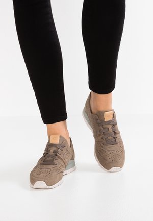 Zapatillas de ante gris con detalles perforados, diseño de cordones y una suela crema moteada. Presenta un acento del logo en la lengüeta.