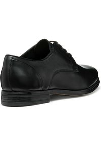 Scarpa elegante nera in pelle con finitura lucida, punta tondeggiante, design con lacci e suola piatta. Tacco leggermente imbottito per il comfort.