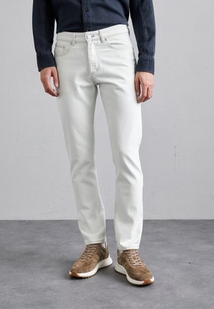 Jeans de mezclilla de color claro con un corte recto, bolsillos frontales y costuras sutiles. Combinados con zapatillas de ante marrón.