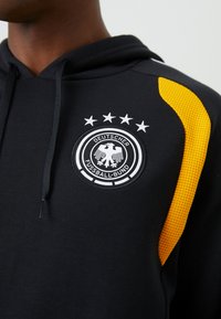 Sweatshirt preto com um destacado logótipo circular bordado com uma águia, quatro estrelas acima e um detalhe texturizado amarelo no ombro.
