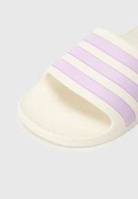 Sandália de slide branca com acabamento texturizado, com três riscas horizontais em lavanda. Design de biqueira aberta com sola flexível e moldada.
