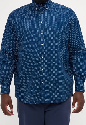 Homme portant une chemise bleu marine à manches longues boutonnée avec de petits pois blancs et un pantalon bleu marine assorti.