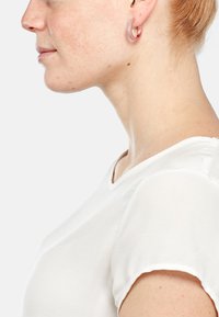 Runde Creolen mit pinkfarbener Metalloberfläche und eingelegten klaren Steinen, getragen mit einem weißen Kurzarmoberteil, im Profilansicht dargestellt.